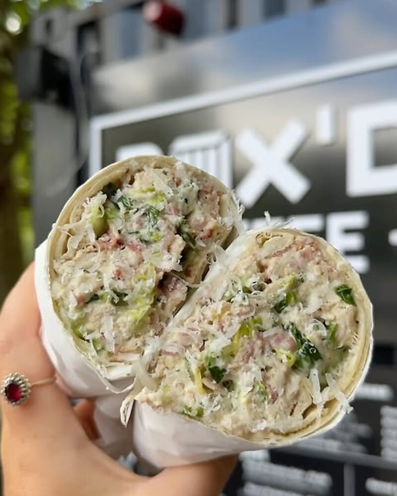 A Caesar wrap cut in half, held up in front of the Box'd container sign