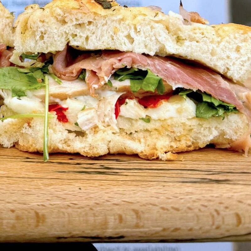 A cut focaccia sandwich with prosciutto, rocket and roasted red pepper