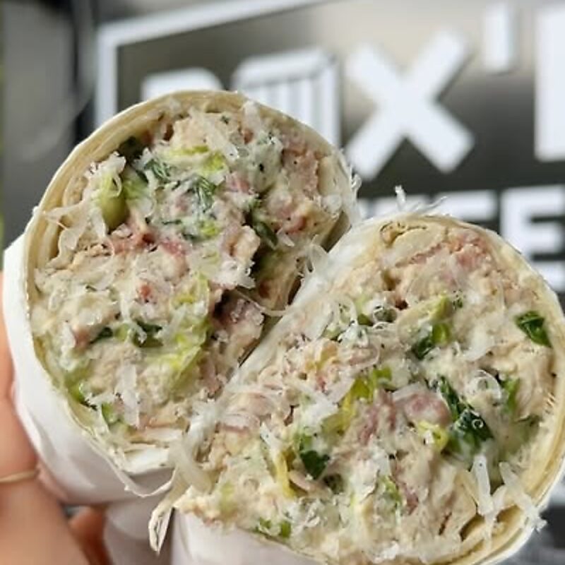 A Caesar wrap cut in half and held up in paper